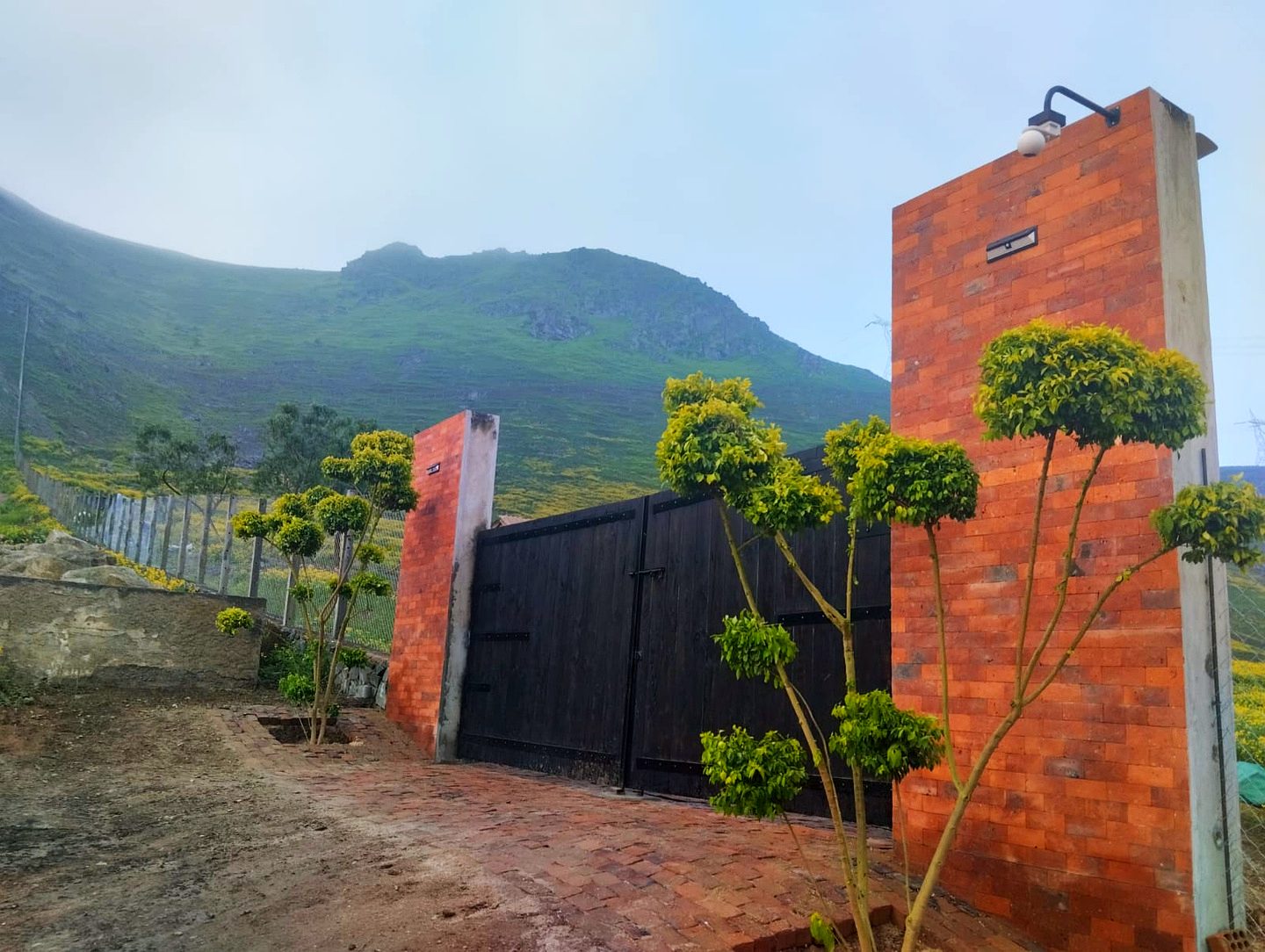 Pórtico de ladrillo cara vista del condominio Alta Colina, con el cerro verde y la neblina de fondo